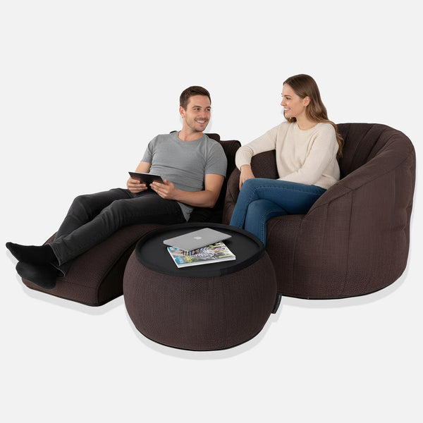 Mies ja nainen istuvat mukavasti Loft-paketin ruskeilla papupussituoleilla, ja heidän välissään on pyöreä ottomaani, jossa on kannettava tietokone ja lehtiä. He hymyilevät toisilleen muodostaen viihtyisän sittegruppen valkoista taustaa vasten.