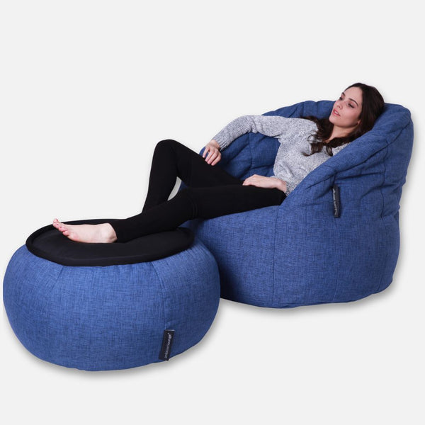 Nainen löhöilee mukavasti Ambient Lounge Cove Package -paketin päällä, ja hänen jalkansa lepäävät yhteensopivalla sinisellä ottomaanilla - suunnittelijan sittegruppe, joka on asetettu valkoista taustaa vasten.