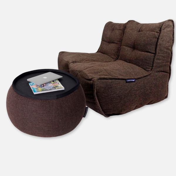 Ruskea, pehmustettu Twin Couch -kaksipaikkainen sohva ja siihen sopiva pyöreä ottomaanipöytä. Ihanteellinen SOHO-pakken, fleksible møbler muotoilu on litteä musta tarjotin ottomaanissa, jossa on suljettu kannettava tietokone ja aikakauslehti, jossa on pehmeä, kankainen rakenne.