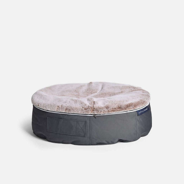 Ambient Loungen pyöreä, harmaa hundeseng, jonka päällä on pehmeä, vaaleanruskea tekoturkki, joka tarjoaa optimaalisen mukavuuden hundille, istuu tavallisella valkoisella pohjalla.