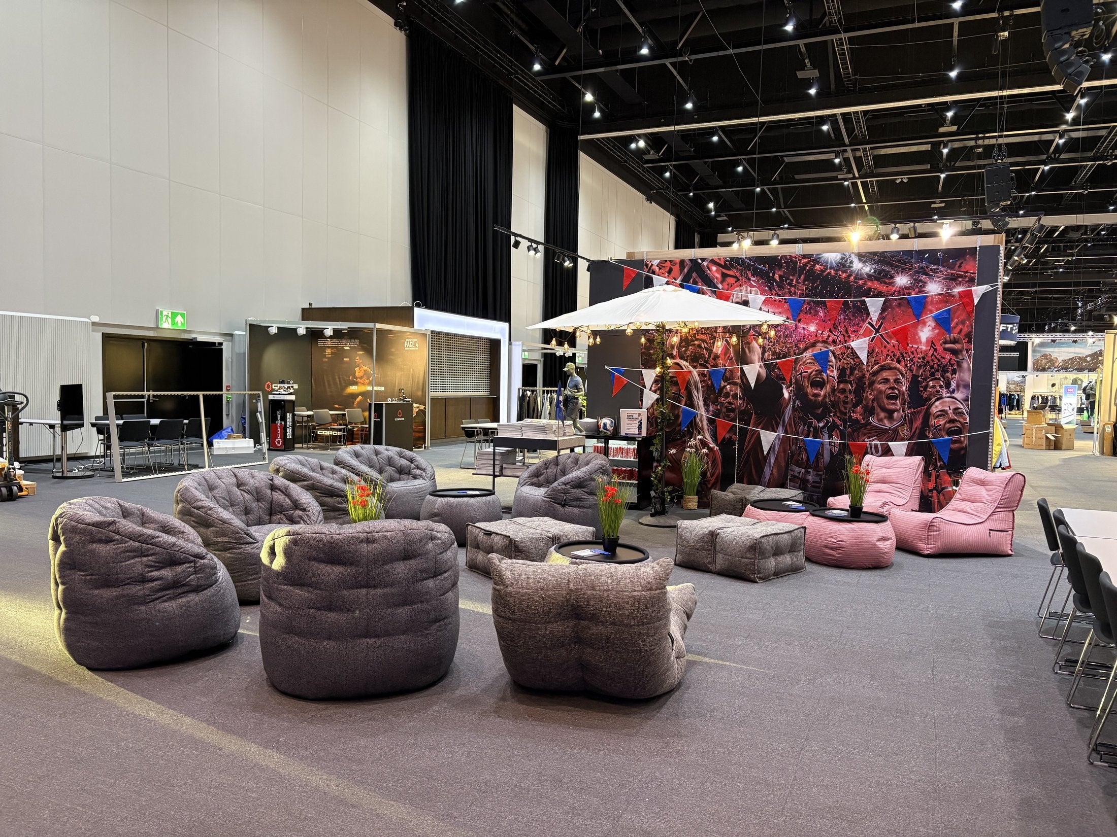 Sommerlounge fra Ambient Lounge på Intersports innkjøpsmesse – grå Acoustic-loungere og Butterfly-sofaer med rosa Raspberry-detaljer under en lys baldakin i messehallen på Thon Hotel Gardermoen.